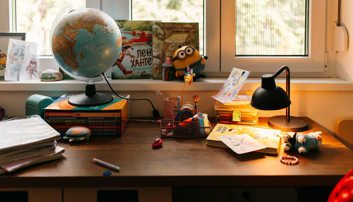 Desk with globe and toys beside books and papers in a well lit room